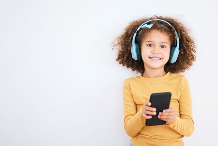 Girl kid, portrait and smartphone, headphones and music with smile isolated on white background....