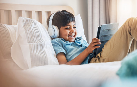 Child, tablet and smile with headphones on bed for online games, watch movies or play educational...