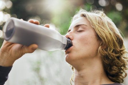 Health, fitness and drinking water with man in nature for workout, exercise and sports. Wellness, marathon and training with face of person and bottle in forest for cardio, challenge and performanceの写真素材