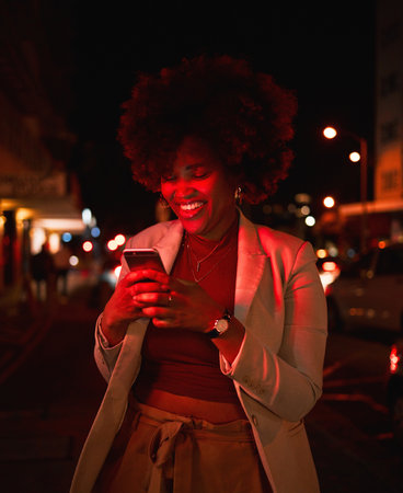 Happy black woman, afro and phone at night in city for communication, social media or outdoor networking. African female person smile in online chatting or late evening on mobile smartphone in townの写真素材