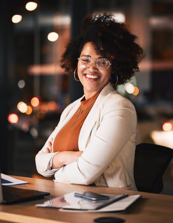 Night, portrait and a black woman with arms crossed at work for business pride or a deadline. Desk, happy and an African employee with confidence during overtime and late shift in the officeの写真素材