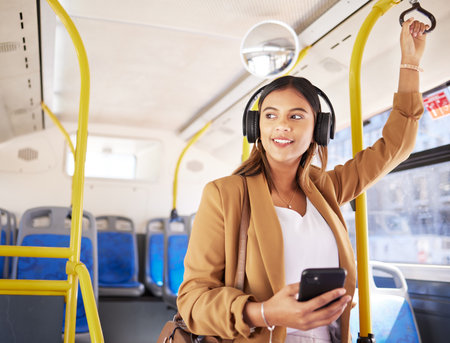 Bus, woman and phone with headphones on public transport, music and smile with business commute. City travel, stop and internet app of a female professional on a mobile with networking on metroの写真素材