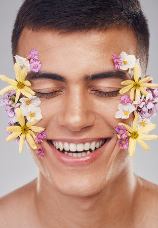 Relax, face or happy man with flowers for beauty, natural cosmetics or wellness in studio on white background. Nature aesthetic, smile or model laughing at eco friendly skincare or spring floral artの写真素材