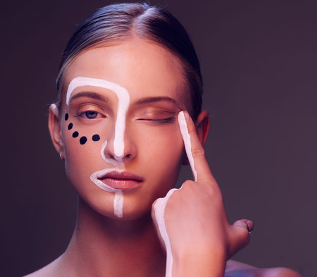 Woman, skin and paint in studio, wink and closeup for art, wellness or fantasy with cosmetic by dark...