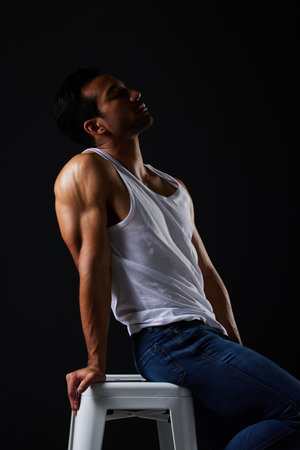 Sexy, muscle and man on chair in studio with fitness inspiration, beauty aesthetic and sensual fashion. Erotic art, sexual body and male model sitting on black background, thinking in dark lighting.の写真素材
