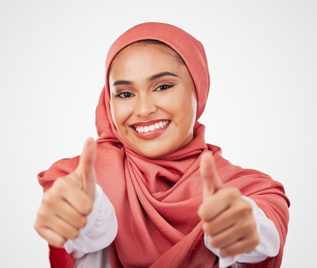 Muslim, woman and thumbs up, hands and agreement with smile in portrait isolated on white background. Hijab, opinion with communication and success, support and like emoji with vote in a studioの写真素材