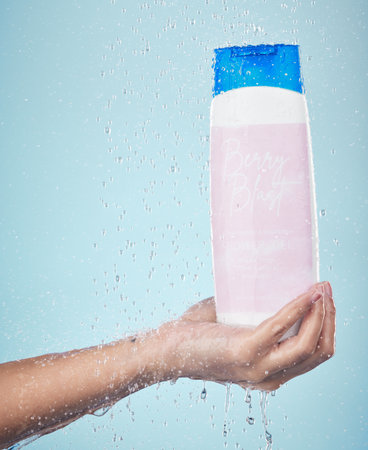 Person, hand and shower gel with product in hygiene, washing or cleanse against a blue studio background. Closeup of model holding skin cosmetics, soap or body care with water drops in bathroomの写真素材