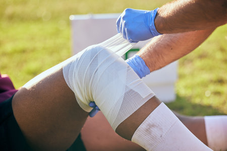 First aid, sport injury and leg bandage with soccer accident, fitness and massage on a field. Training, workout and physical therapy of knee pain at game with healthcare emergency from exerciseの写真素材