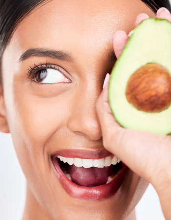 Closeup, avocado and happy woman with natural beauty, face and eco friendly skincare on white background. Wellness, dermatology and vegan cosmetics product with glow, facial and green in a studioの写真素材
