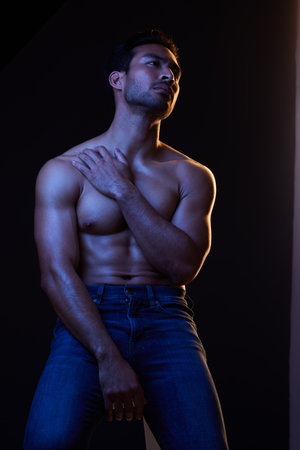Sexy, muscle and man with fitness, wellness and posing on a dark studio background. Person, guy and model with jeans, shirtless and atmosphere with training, power and body goals with aestheticの写真素材