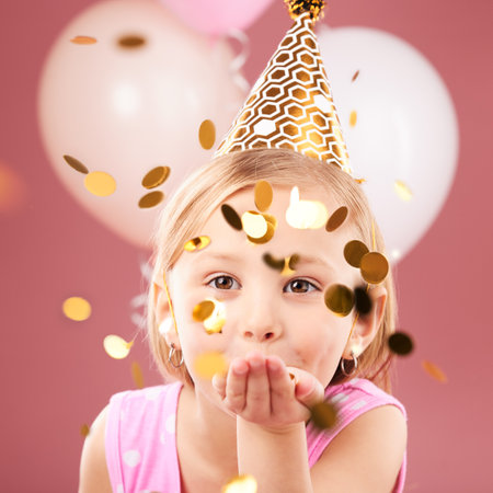 Balloons, birthday and portrait of girl with confetti on pink background for party, celebration and special day. Happy, excited and young child with decoration for magic, wonder and glitter in studioの写真素材