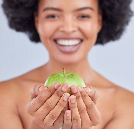 Apple, black woman and hand closeup with health, diet and natural skincare glow in studio. Happy, face and fruit for healthy nutrition, grey background and wellness with a smile from organic foodの写真素材