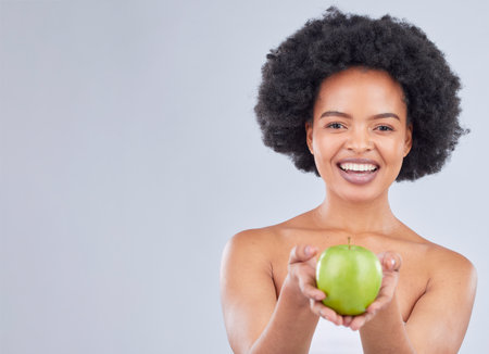 Apple, black woman and portrait with health, diet and natural skincare glow in studio. Happy, face and fruit for healthy nutrition, grey background and mockup space with a smile from organic foodの写真素材