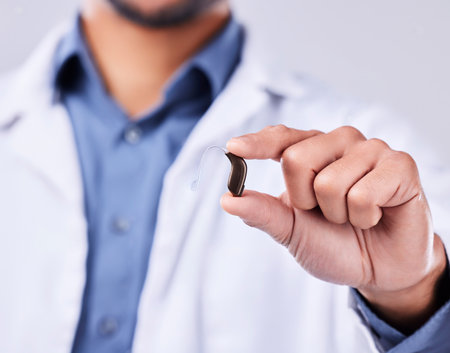 Closeup, hand and a hearing aid from a doctor for communication, medical support or service. Healthcare, sound and a person or surgeon with an ear piece for listening, audiology or helping with gearの写真素材