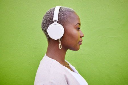 Music headphones, profile and black woman listening on green wall background mockup space. Radio, serious and African person streaming podcast, hearing audio and sound of jazz media on technology.の写真素材