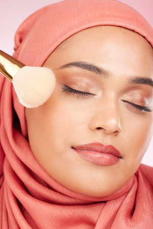 Makeup brush, relax and muslim woman closeup with a smile from cosmetics and blush in studio. Facial, glow and happy female person with beauty, skincare and shine with a hijab and skin tool for faceの写真素材