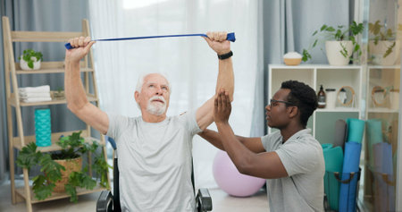Man with disability, physiotherapist and stretching band for healthcare rehabilitation, consulting and physical therapy assessment. Clinic, physiotherapy and support for senior patient in wheelchairの写真素材