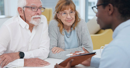 Senior couple with a male financial advisor by a table in the dining room of their modern house. Conversation, meeting and elderly man and woman planning their retirement fund with accountant at homeの写真素材