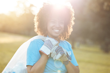 Nature portrait, community volunteer and happy woman cleaning garbage, eco waste and plastic trash. Sunshine, NGO service and activist support park clean up, outreach project or environment pollutionの写真素材
