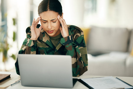 Headache, stress or woman soldier with trauma and depression at desk with anxiety on laptop. Frustrated, psychology or sad person with army memory, military frustration or ptsd crisis typing onlineの写真素材