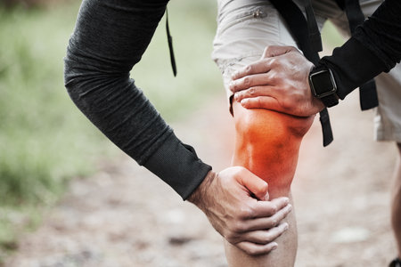 Knee pain, injury and red inflammation and person hand with fitness, workout and training accident from hike. Runner, leg massage and trekking in the woods on trail with muscle strain and emergencyの写真素材