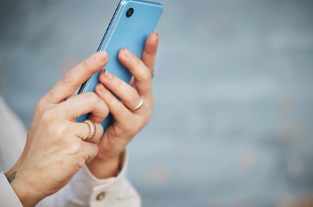 Hands, phone and space with a person closeup on a blurred gray background for social media, communication or networking. Mobile, contact and app with an adult typing or reading a text messageの写真素材