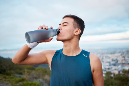 Man, fitness and drinking water in nature, workout or outdoor exercise on break, rest or recovery. Thirsty male person, sports drink or mineral for sustainability after running, cardio or trainingの写真素材