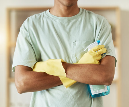 Man, hands and spray bottle in housekeeping, cleaning or bacteria and germ removal at home. Closeup of male person, maid or cleaner with arms crossed of professional in domestic service at houseの写真素材