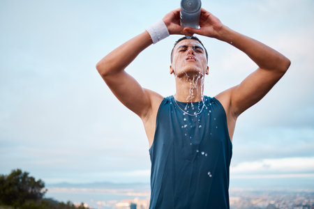 Exercise, water and fatigue with a sports man outdoor, tired after running a marathon for cardio training. Fitness, health and an exhausted young runner pouring liquid for hydration or refreshmentの写真素材