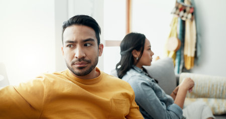 Couple, fight and angry in home for divorce, breakup and ignore partner in bad argument on sofa. Asian man, woman and thinking of stress, conflict and drama of cheating, mistake or toxic relationshipの写真素材