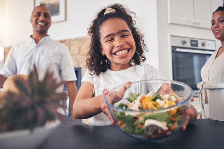Child, smile and dinner table with salad, healthy food and thanksgiving meal with family at home. Happy, young girl and giving at a holiday with portrait and parents at lunch with people togetherの写真素材