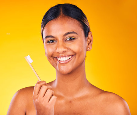 Woman, toothbrush in portrait with smile and dental in studio, health and wellness on yellow...