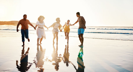 Friends, running and people happy at sunset beach for fun, freedom and travel with care. Diversity, men and women group holding hands in nature with sand, love and happiness on a vacation or holidayの写真素材