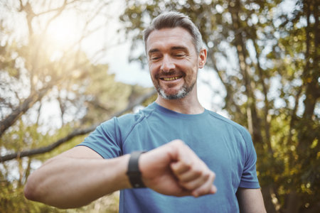Happy runner man, smart watch and park for check, smile or reading for time, results or fitness in nature. Person, iot clock and monitor for speed, heart rate or smile for exercise, workout or healthの写真素材