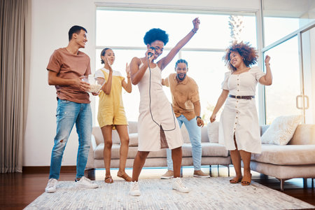Sing, energy and friends dancing in the living room with a microphone to music, playlist or radio. Happy, diversity and young people moving, bonding and having fun together with karaoke at home.の写真素材