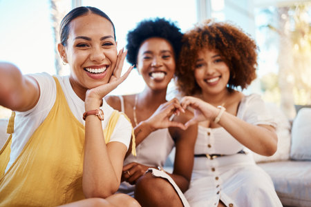Portrait, heart hands and selfie of friends in home living room, bonding and having fun on sofa. Face, profile picture and love sign of group of women in photography, happy memory and emoji for careの写真素材