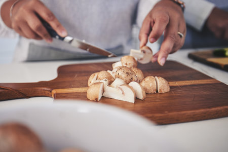 Cut, mushroom and person hands cooking vegetable in a kitchen on a board or table in a home as healthy a chef. Salad, food and woman prepare produce for a supper, lunch or dinner for diet mealの写真素材