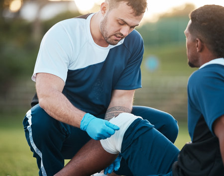 Sports, injury and man on field with bandage for accident, emergency and first aid for muscle sprain. Fitness, healthcare and medic with athlete with knee pain from exercise, workout and trainingの写真素材