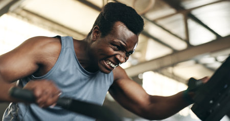 Black man, fitness and cycling at gym in cardio workout, exercise or intense training on machine. African male person on bicycle equipment in sweat or running for muscle, endurance or stamina at clubの写真素材