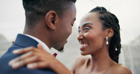 Outdoor, kiss and black couple with marriage, wedding and hug with happiness, romance and celebration. African man, happy woman and embrace outside, love and bride with groom, romantic and commitmentの写真素材