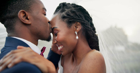Outdoor, kiss and black couple with love, wedding and hug with marriage, happiness and celebration. African man, happy woman and embrace outside, event and bride with groom, romance and countrysideの写真素材