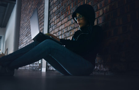 Hacker, woman in dark room with laptop and information technology, phishing and cyber crime with database or server. Cybersecurity, programming and criminal with pc, ransomware and firewall breachの写真素材