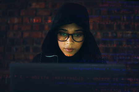 Hacker, woman in basement and laptop, coding and IT with code overlay, database with phishing and cyber crime. Cybersecurity, programming or hacking, criminal with pc for ransomware and firewallの写真素材