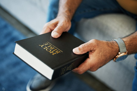 Bible, book and hands of man in home with study of Christian faith, religion or spirituality...