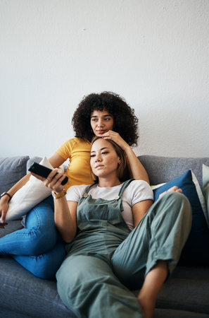 Love, television and a lesbian couple watching a movie on a sofa in the living room of their home together. Relax, LGBT and a woman with her girlfriend enjoying series on a streaming serviceの写真素材