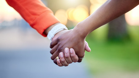 Interracial couple, holding hands and love in nature for support, trust or unity together. Closeup of people touching in romance, care or friendship walk in an outdoor park for partnership or duoの写真素材