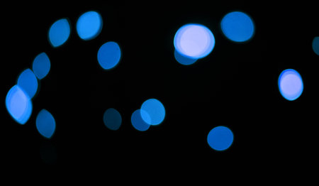 Blue, lights and bokeh in a studio with dark background for celebration, event or party. Confetti, glitter and color sparkles for magic, shine or glow for festive by black backdrop with mockup.の写真素材