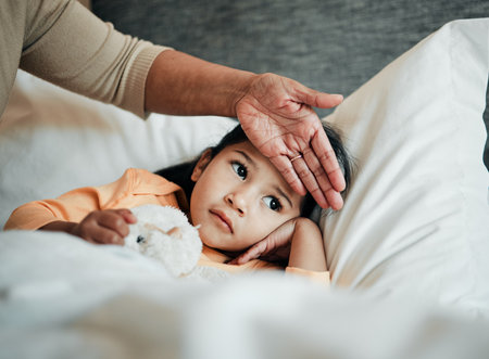 Girl kid, check for fever and sick in bed with hand on head, health and wellness, parent monitor temperature at home. Headache, illness and young child with the flu, medical help and support of momの写真素材