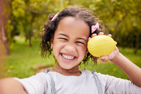 Selfie, portrait and girl child with fruit and smile in nature for wellness, nutrition and healthy lifestyle. Face, kid and person with lemon in hand for summer, eating and happiness outdoor on farmの写真素材