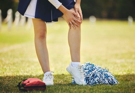 Cheerleader, injury and person with knee pain from sport, training and cheer exercise on a grass...